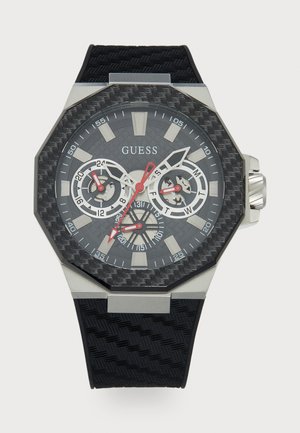 Octagonale horloge met een getextureerde zwarte carbonfiber wijzerplaat, zilveren en rode accenten, drie sub-dials en een zwarte rubberen band.
