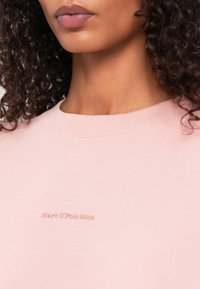 Felpa rosa chiaro con scollatura tonda, caratterizzata da un logo in rilievo "Marc O'Polo DENIM" dello stesso colore per un dettaglio discreto. Texture morbida.