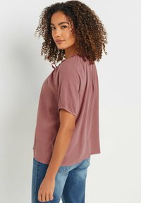 Krótki rękaw różowa bluzka z marszczonym dekoltem, miękka w dotyku i luźno dopasowana, w połączeniu z jasnoniebieskimi dżinsami.