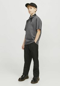 T-shirt di cotone grigia, slim fit, abbinata a pantaloni neri. Gli accessori includono un cappellino nero e un bandana nera legata attorno al collo.