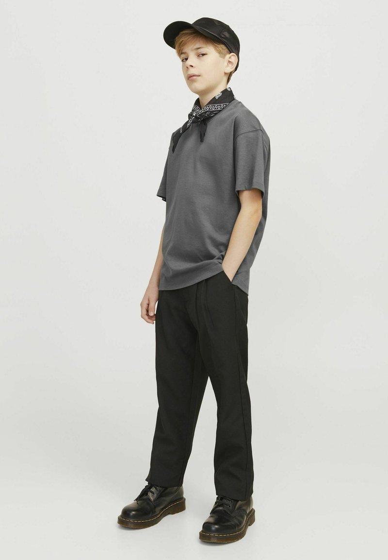 T-shirt di cotone grigia, slim fit, abbinata a pantaloni neri. Gli accessori includono un cappellino nero e un bandana nera legata attorno al collo.