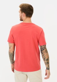 Rød bomulds t-shirt med en klassisk rund halsudskæring, korte ærmer og en glat tekstur. Viser synlige tatoveringer på venstre arm.