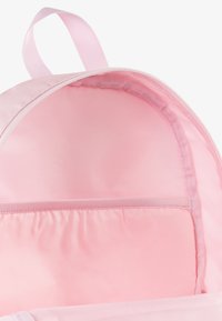 Innvendig i den rosa ryggsekken har en glatt, blank tekstur. Den har en elastisk lomme og matchende stofffor, designet for å organisere gjenstander.
