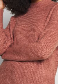 Texturerad stickad tröja i rosaröd, med hög hals, långa ärmar och ribbade detaljer över hela tyget.