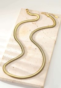 Gold-tone snake chain necklace, flexible with a textured surface, featuring a closure and extension chain. Displayed on a light-colored surface.