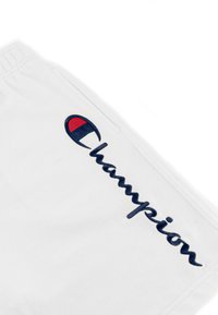 Prenda de algodón blanca con un gran bordado en azul marino de "Champion" acompañado de un acento en rojo y azul. Textura suave y diseño casual.