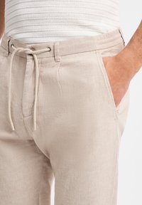 Beige linnen broek met een elastische tailleband met trekkoord, zijzakken en een lichte, gestructureerde stof.