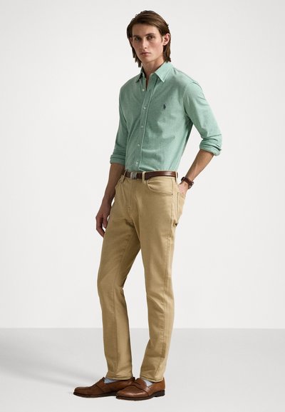 Groene overhemd, tan chino's, bruine schoenen. Het overhemd heeft een slim fit en kraag; de chino's zijn recht. Een brown riem voegt contrast toe.