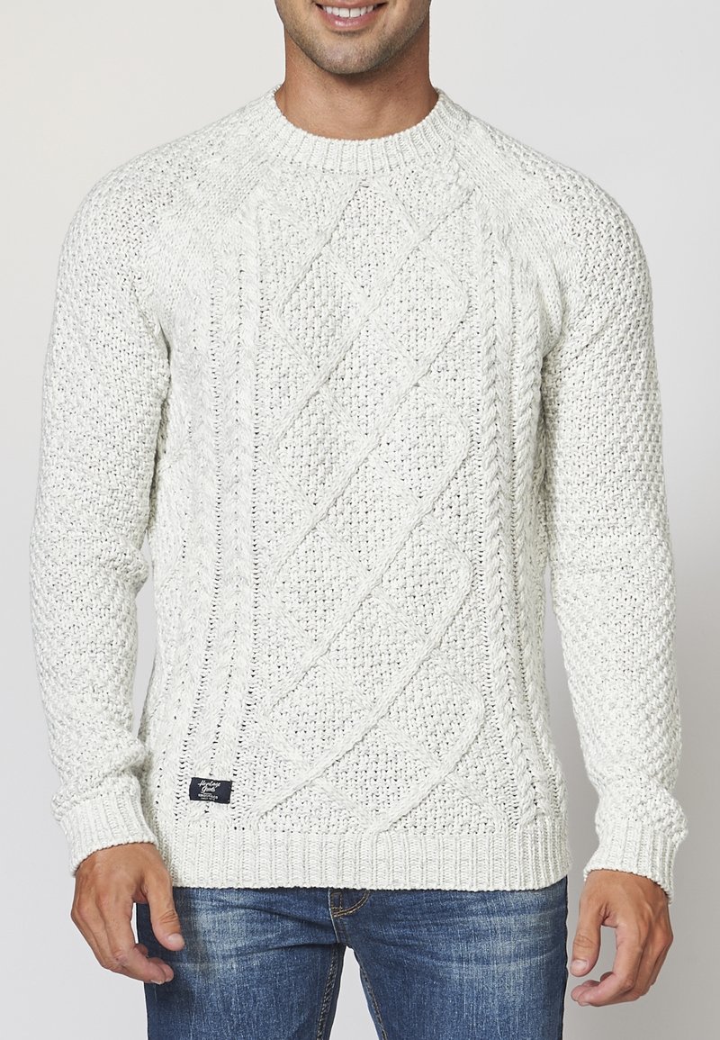 Krämfärgad stickad tröja med kabelmönster, rund halsringning och ribbade muddar och nederkant. Texturerad garn, strukturerad passform, avslappnad stil.