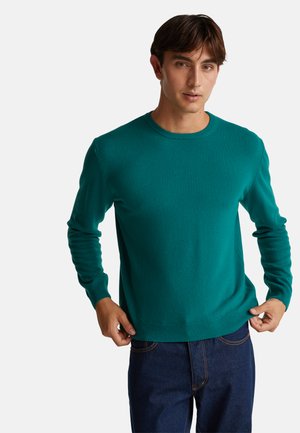 Maglione verde a collo rotondo realizzato in tessuto liscio, dal taglio aderente con maniche lunghe e polsini a coste, abbinato a jeans blu scuro.