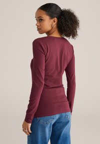 Dlhý rukáv burgunský top vyrobený z mäkkej tkaniny, priliehavý strih s okrúhlym výstrihom, skombinovaný s vysokým pásom modrými džínsami.