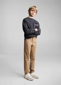 Sweat-shirt gris avec logo, pantalon beige et baskets claires. L'ensemble présente une coupe décontractée et des textures contrastées dans les matériaux.