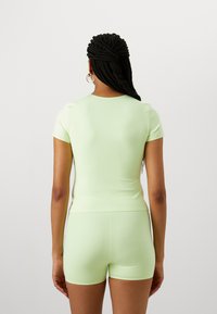 Ljusgrön tränings-topp med korta ärmar och figurnära design, tillsammans med matchande shorts. Slät textur, minimalistisk stil, inga synliga mönster.