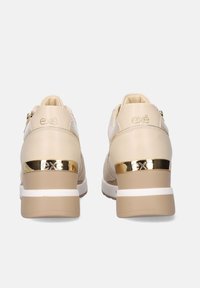Zapatillas beige con acabado texturizado, con un acento dorado en el talón, una entresuela blanca y un logotipo en la parte posterior.