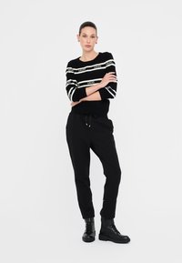 Maglione nero a maglia con strisce bianche e dettaglio del logo, abbinato a pantaloni neri a sigaretta e stivaletti neri con lacci e suola spessa.