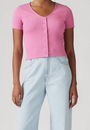 Kort roze geribd crop top met een diepe V-hals en zes bijpassende knopen aan de voorkant, gecombineerd met lichtblauwe jeans met hoge taille.