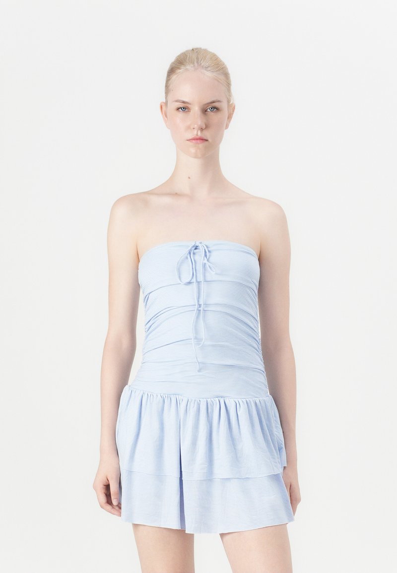 Šviesiai mėlyna be petnešų suknelė, pagaminta iš minkštos medžiagos, su susiraukusiu liemeniu, pririšimo detale priekyje ir sluoksniuotomis raukšlių sijonais.