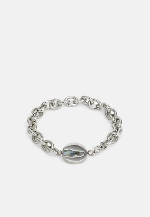 Sidabrinė grandinėlė su ovaliu pakabuku, turinčiu žvilgantį detalų, sujungtu dizainu, blizgiu paviršiumi ir saugiu užsegimu.