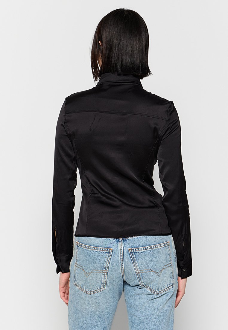 Schwarze Satin-Hemd mit langen Ärmeln, schmaler Passform, Rückennaht und seitlichen Schlitzen, kombiniert mit hellblauen Jeans.