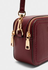 Bordeaux læder crossover taske med guldfarvet hardware, dobbelte lynlåse og en tekstureret finish. Har en kort rem og kontraststing.