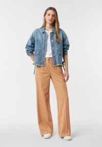 Jasnoniebieska kurtka dżinsowa z naszywanymi kieszeniami, zestawiona z beżowymi szerokimi spodniami i białą koszulą, charakteryzująca się luźnym krojem i podwiniętymi rękawami.