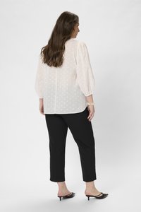 Blouse transparente rose clair avec des pois blancs, manches bouffantes, associée à un pantalon noir slim et des mules noires à talons.