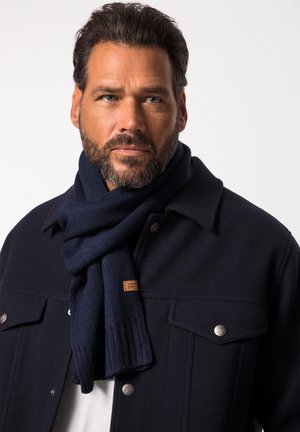 Navy knitted scarf wrapped around the neck, paired with a dark woolen jacket featuring metal buttons and two front pockets.