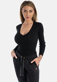 Bodysuit negro de manga larga con acanalado, cuello en V y diseño ajustado, combinado con pantalones jogger negros con cinturilla elástica y cordones.