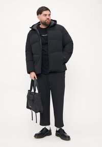 Black puffer jacket with a hood, featuring a quilted design. Worn over a black shirt, paired with loose black pants and black footwear.