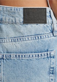 Lichtblauwe denim jeans met een zwart leren label aan de achterkant, voorzien van standaard stiksel en een achterzak.