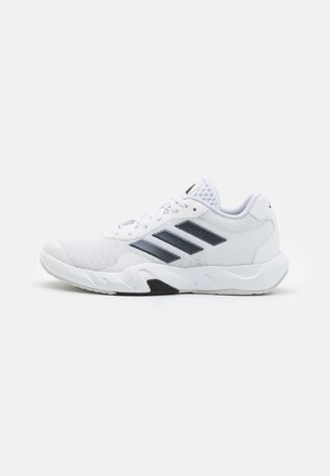 Zapatilla deportiva blanca con parte superior de malla, tres franjas negras a los lados, acentos texturizados y una suela de goma resistente con una sección negra en contraste.