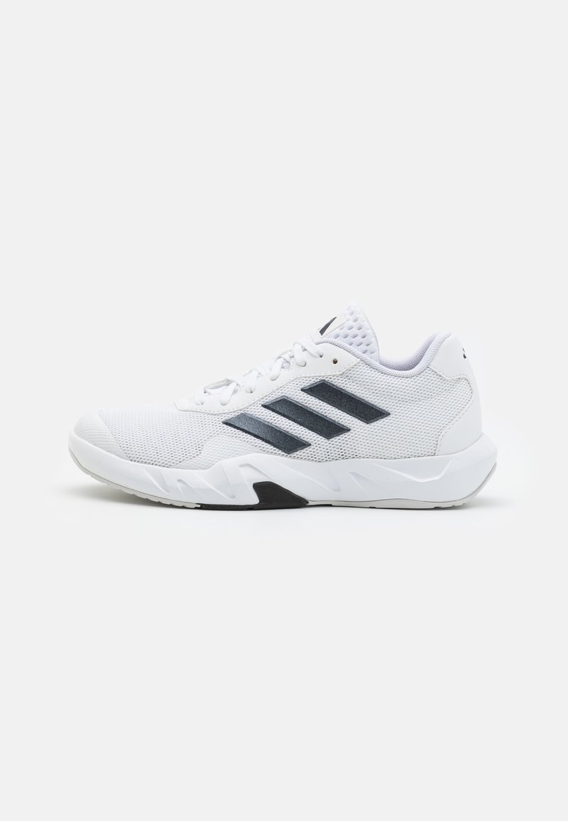 Zapatilla deportiva blanca con parte superior de malla, tres franjas negras a los lados, acentos texturizados y una suela de goma resistente con una sección negra en contraste.