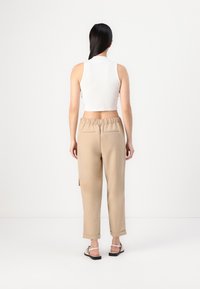 Hvit strikket crop topp med høy hals, parret med beige tapered bukser med snor i midjen og to baklommer.
