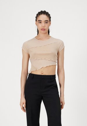 Cropped beige shirt with short sleeves, featuring wavy cut layers and a smooth texture. Paired with black tailored pants.