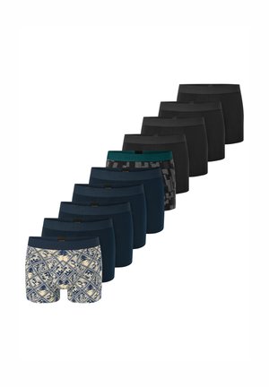 Skjorteløs mand med kort mørkt hår iført sorte og grå mønstrede boxershorts, stående mod en ensfarvet lys baggrund.