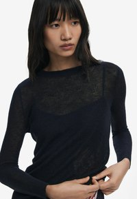 Long-sleeve, navy blue sweater made from a soft, sheer knit fabric. Features a ribbed texture and a fitted silhouette.