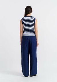 Top senza maniche a righe navy e bianche con bordo a costine, abbinato a pantaloni navy larghi. Design minimalista, texture morbida, senza accenti notevoli.