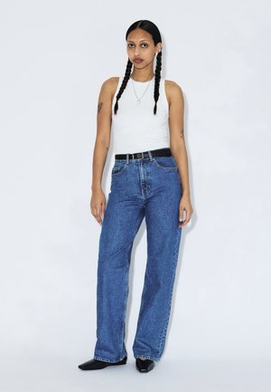 Light blue, high-waisted denim jeans with a straight cut, paired with a fitted white tank top. Features a black belt and sleek black shoes.