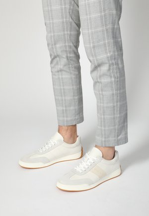 White and gray sneakers with a suede and leather upper, flat laces, a textured sole, and light gum rubber outsole. Plaid gray trousers.