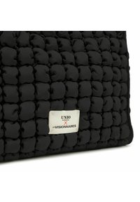 Borsa nera trapuntata con una superficie testurizzata e pomelli arrotondati. Una placca in metallo bianco riporta la scritta "UNIO X LES VISIONNAIRES."