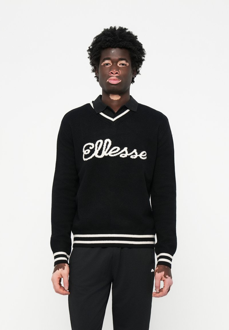 Sort strikket sweater med hvide striber ved ærmer og kant, prydet med et fremtrædende "Ellesse" logo over brystet og en V-halsudskæring.