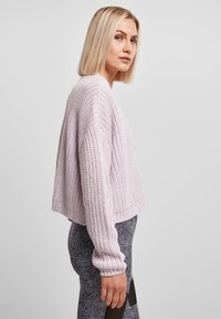 Lys lavendel cropped genser med teksturert strikkemønster og ribbede mansjetter, kombinert med mønstrede tights med svart design.