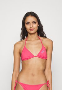 Rosa bikini med triangelformade kupor och justerbara knytband i sidorna. Tillverkad av ett mjukt tyg, med en subtil logotyp i ljusblått på toppen.