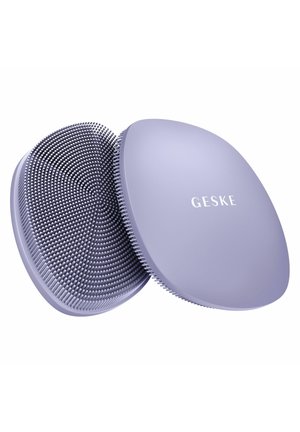 To lilla ovale silikoneansigtsrensningsbørster, den ene med fleksible børstehår, den anden med teksten "GESKE" på den glatte side.