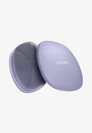 Deux brosses nettoyantes pour le visage en silicone violet ovales, une montrant des poils flexibles, l'autre avec le texte « GESKE » sur le côté lisse.