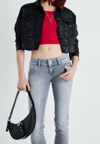 Personne portant une veste noire courte, un haut rouge court, un jean taille haute gris clair, tenant un sac à main noir avec une finition texturée.