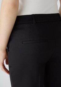 Pantalon noir à la texture lisse, doté d'une poche arrière au design minimaliste. La taille est élastique pour un confort optimal.