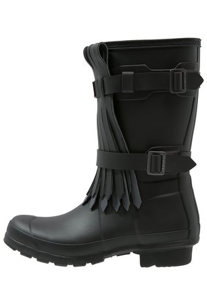 Zwarte rubberen laars tot halverwege de kuit met gespen en gelaagde franjerand aan de zijkant, voorzien van een robuuste zool en een afgeronde neus.