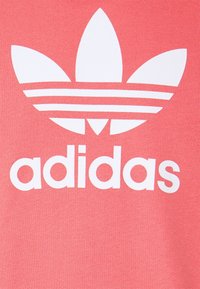Rosa Sweatshirt mit einem großen weißen Adidas-Logo, das drei Streifen darüber und drei blattähnliche Formen aufweist. Der Text ist klar und fett.