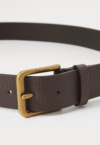 Smeđi kožni remen s teksturiranom površinom, s zlatnom metalnom kopčom. Ime branda "Calvin Klein" uvezeno je blizu kopče.